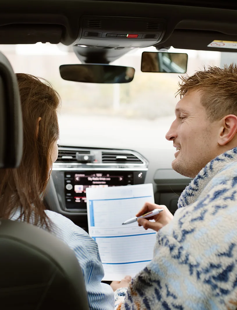 Rij-instructeur neemt het inschrijfformulier door met een leerling in de lesauto