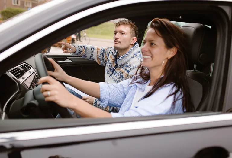 Leerling achter het stuur van de lesauto terwijl de instructeur naast haar de weg aanwijst