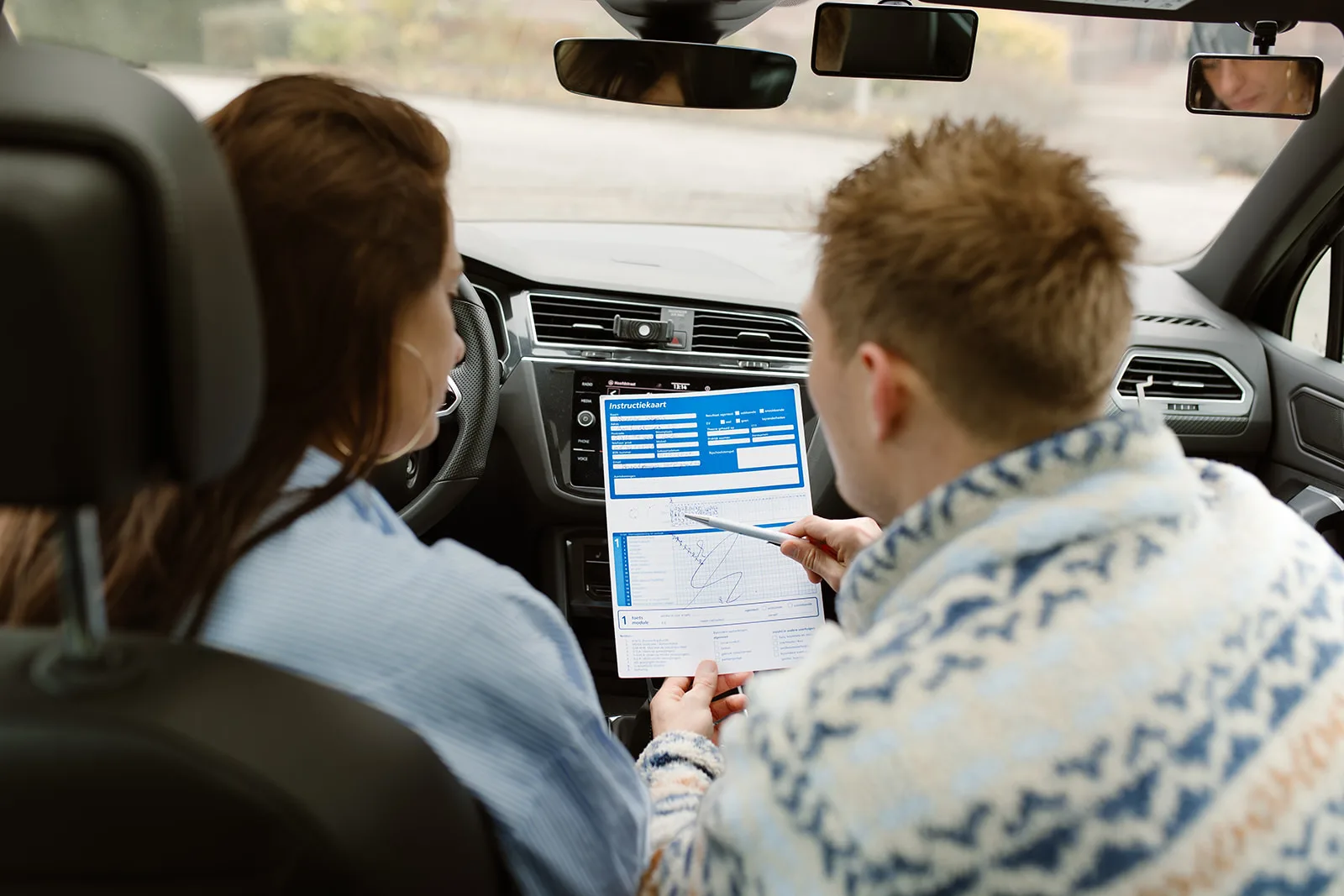Instructeur en leerling bekijken samen het examenformulier in de auto
